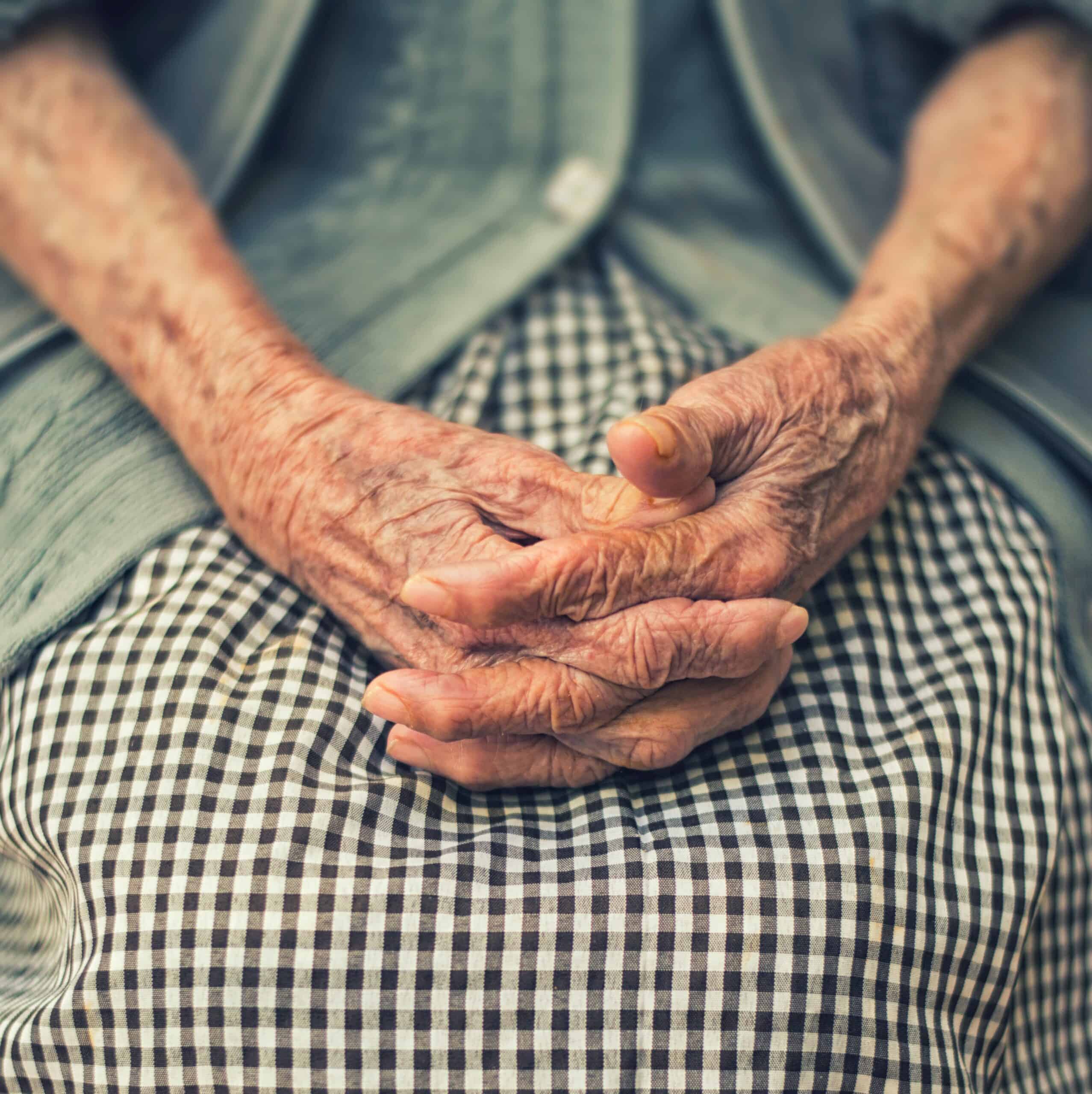 An older lady with frailty hold her hands together