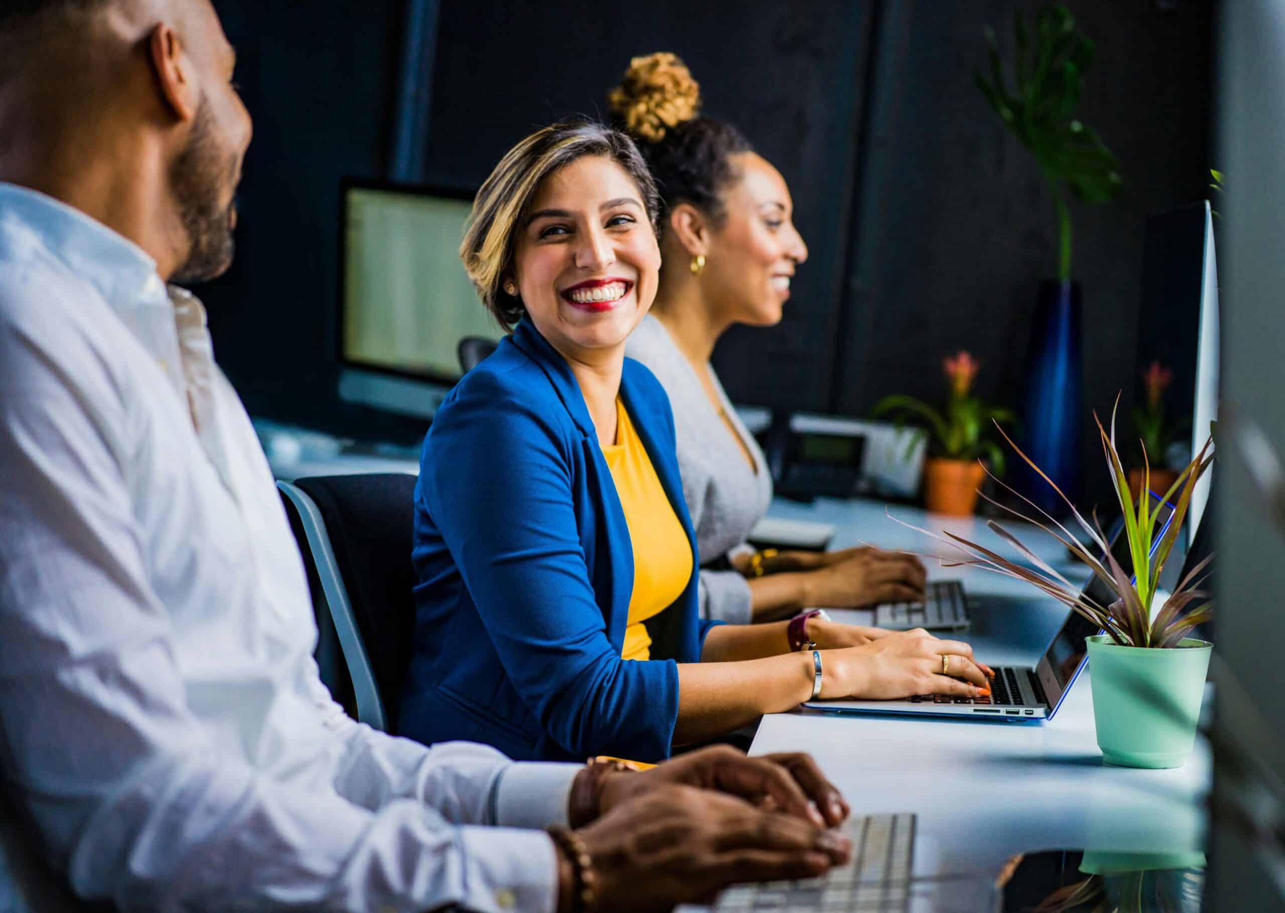 Two women and a man smiling at their computer desks