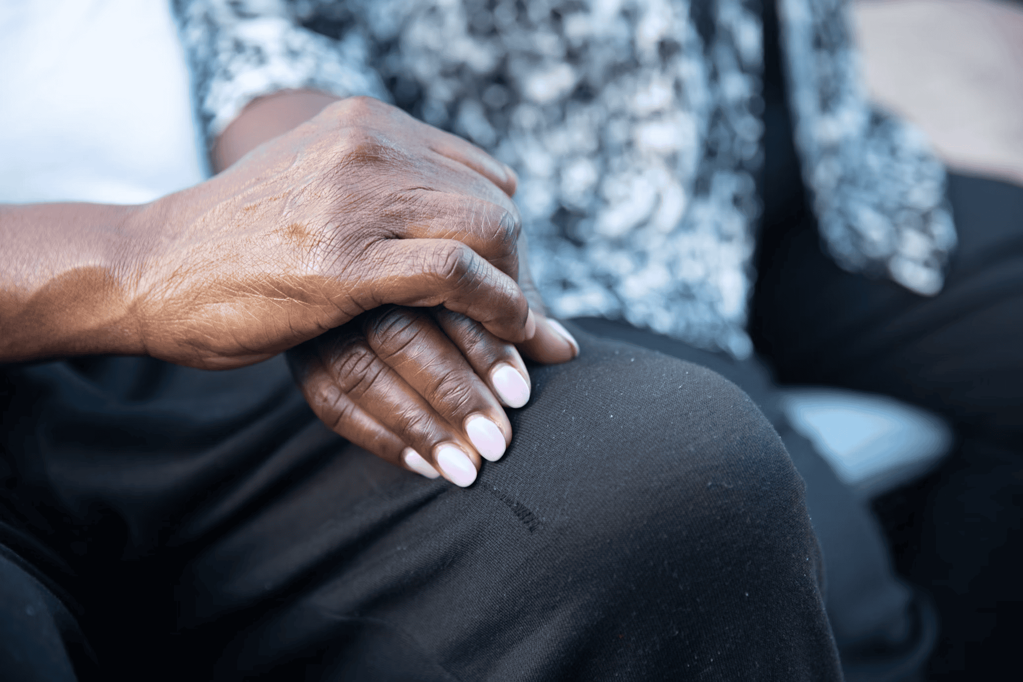 An older man's hand on top of an older woman's hand resting on the man's knee.