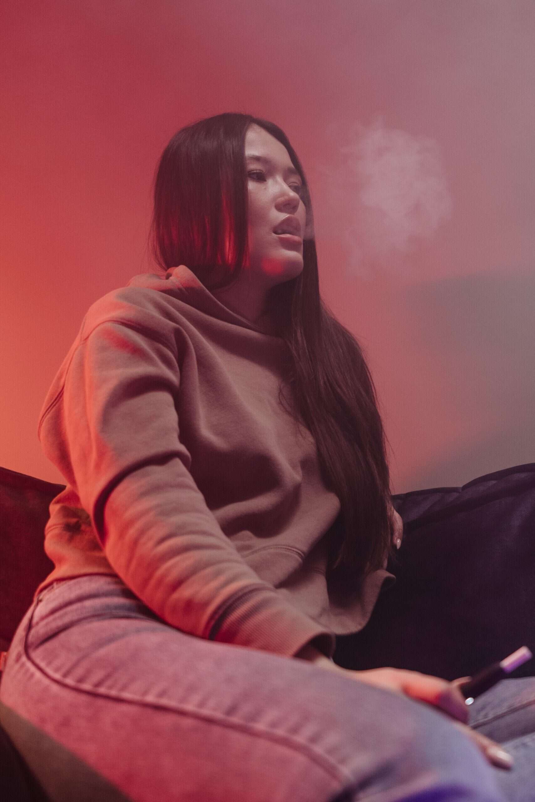 Asian woman sitting on a sofa vaping with smoke coming out her mouth